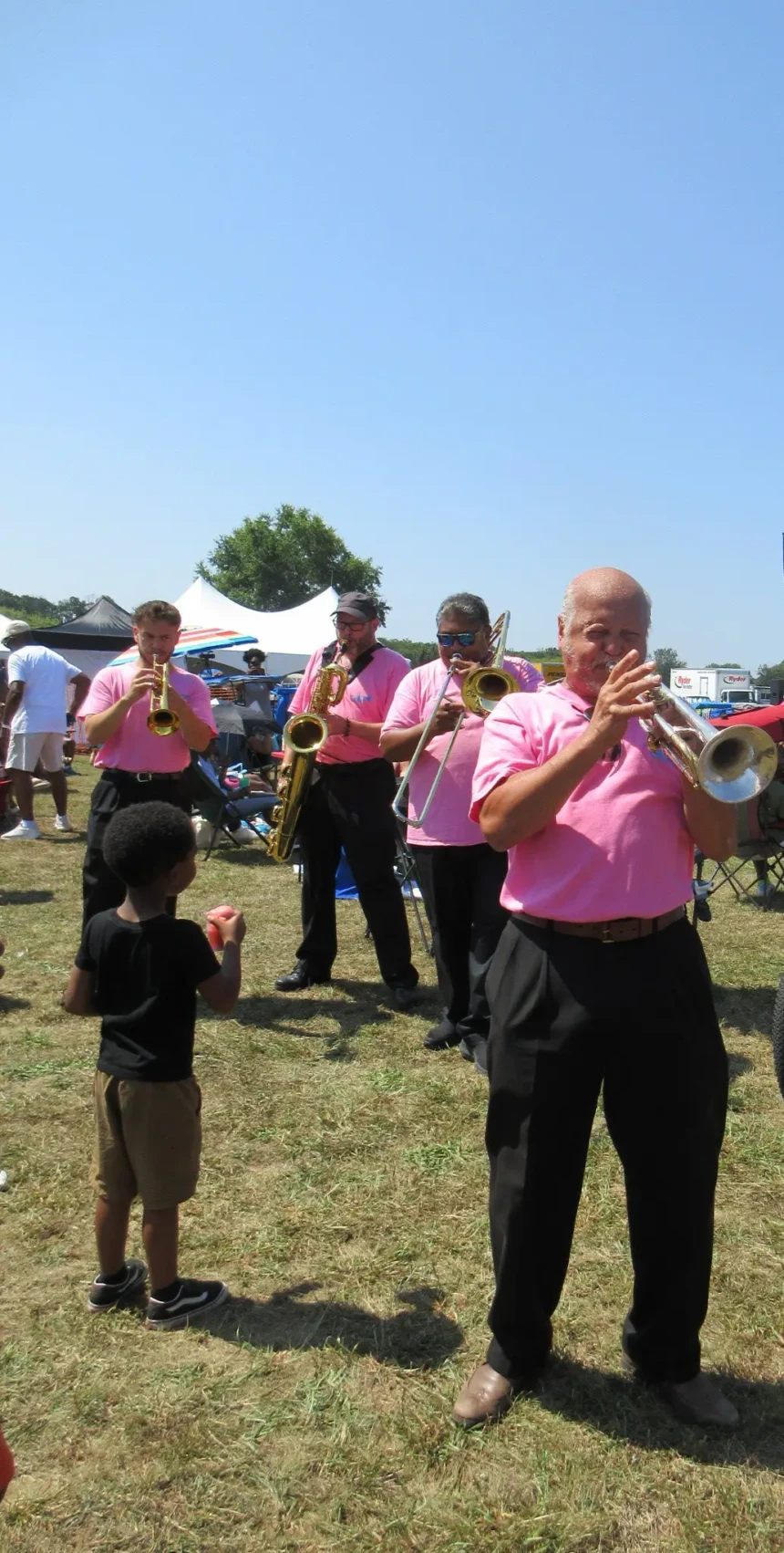Local brass musicians performing among attendees and families at the Willingboro Jazz Festival on a sunny summer afternoon.
