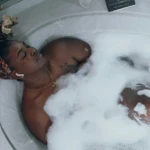 Black woman relaxing in a bubble bath with headphones, practicing self-care