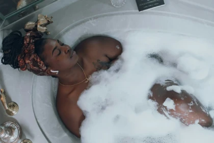Black woman relaxing in a bubble bath with headphones, practicing self-care