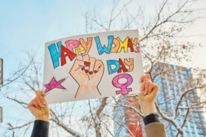 International Women’s Day: Celebrating Progress and Possibility 3 Hands holding a colorful Happy Women's Day sign