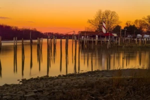 Sunset over the Delaware River at Curtin’s Wharf and Marina in Burlington City, with calm water reflecting dock pilings and a lighthouse-style marina building