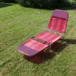 Vintage red woven lawn chair sitting in a backyard, evoking nostalgic summer memories of family gatherings and childhood weekends at grandparents’ homes.