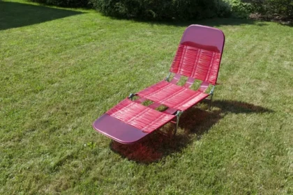 Vintage red woven lawn chair sitting in a backyard, evoking nostalgic summer memories of family gatherings and childhood weekends at grandparents’ homes.