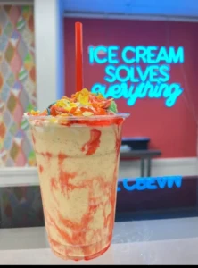 A specialty milkshake sits on the counter inside The Ice Cream Boutique in Bordentown, with a neon sign reading "Ice Cream Solves Everything" in the background.