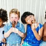 Children eating ice cream cones on a sunny day.